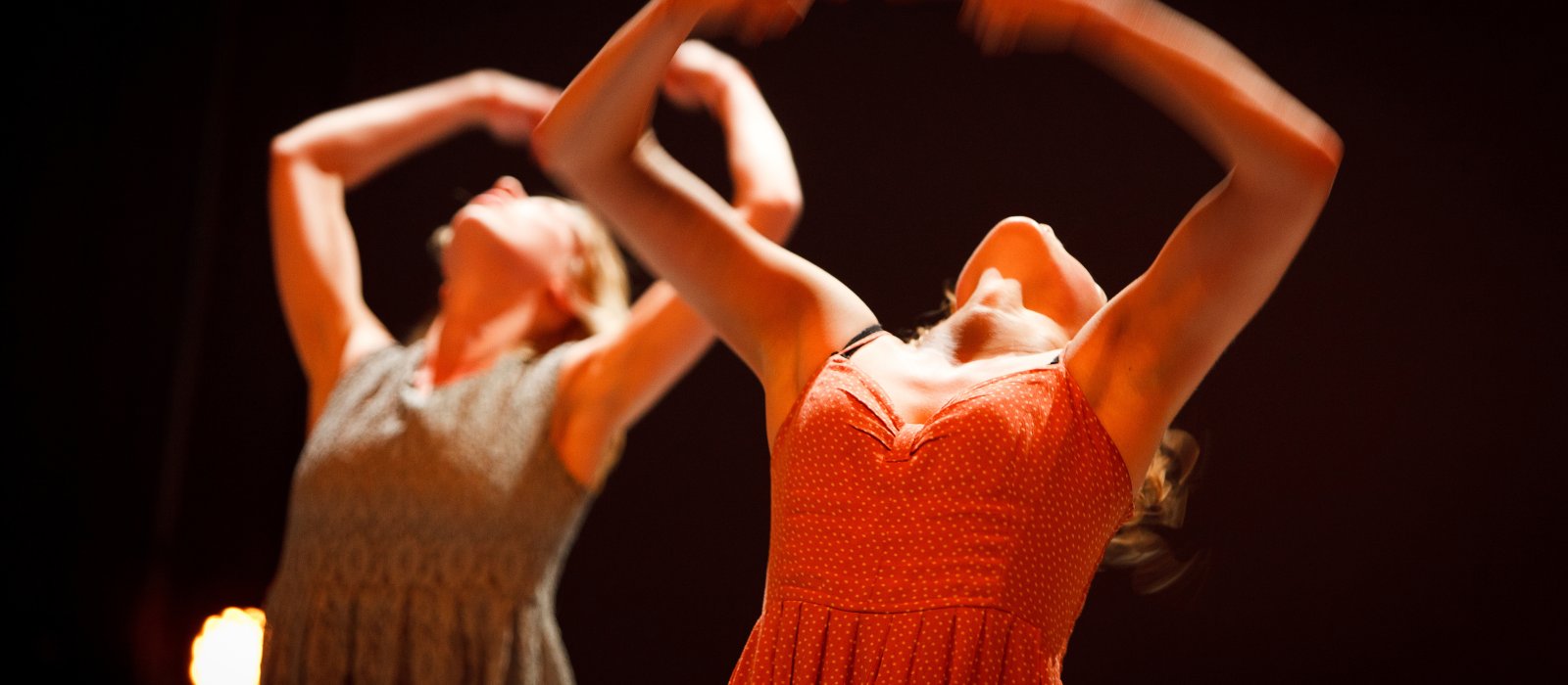 Dancers in dresses throwing hands and heads backwards.