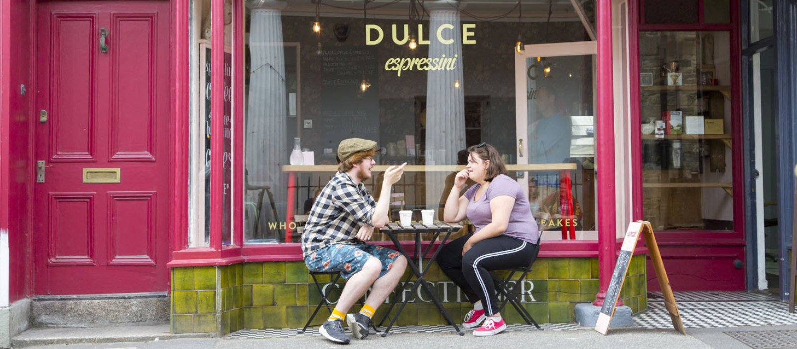 Two Falmouth University students having coffee outside a pink coffee shop