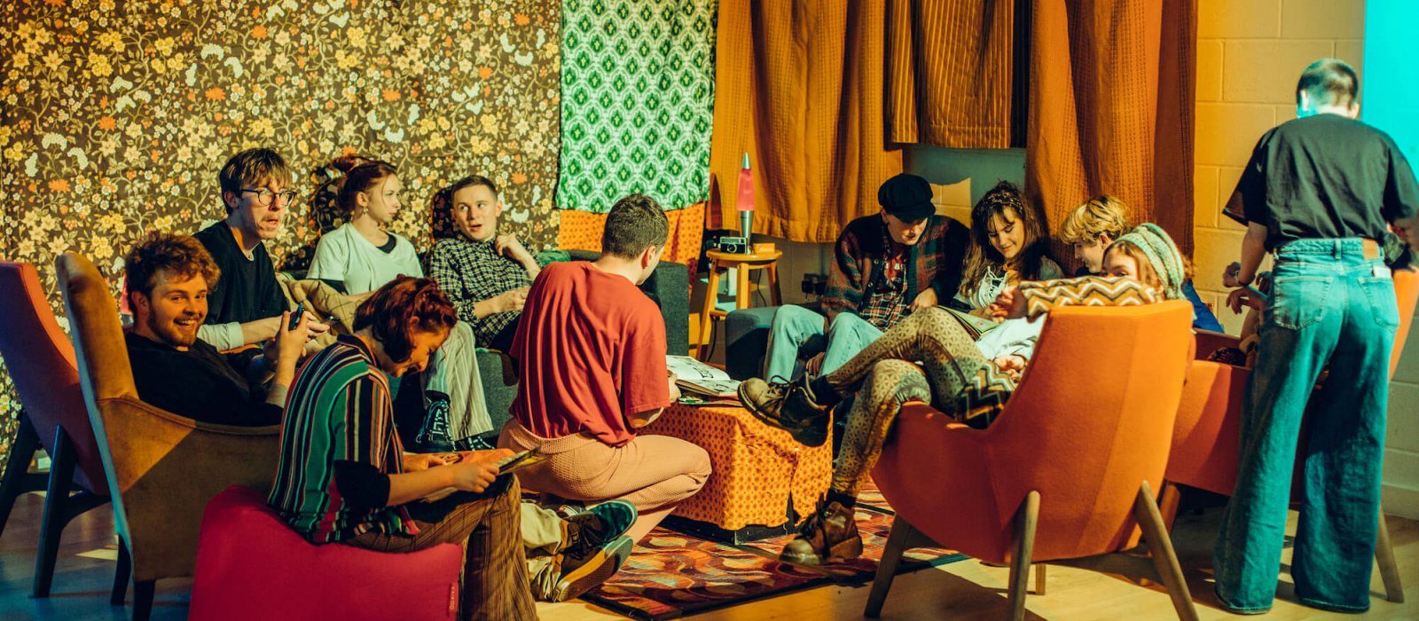 Group of Falmouth students sitting in seventies inspired space with orange curtains