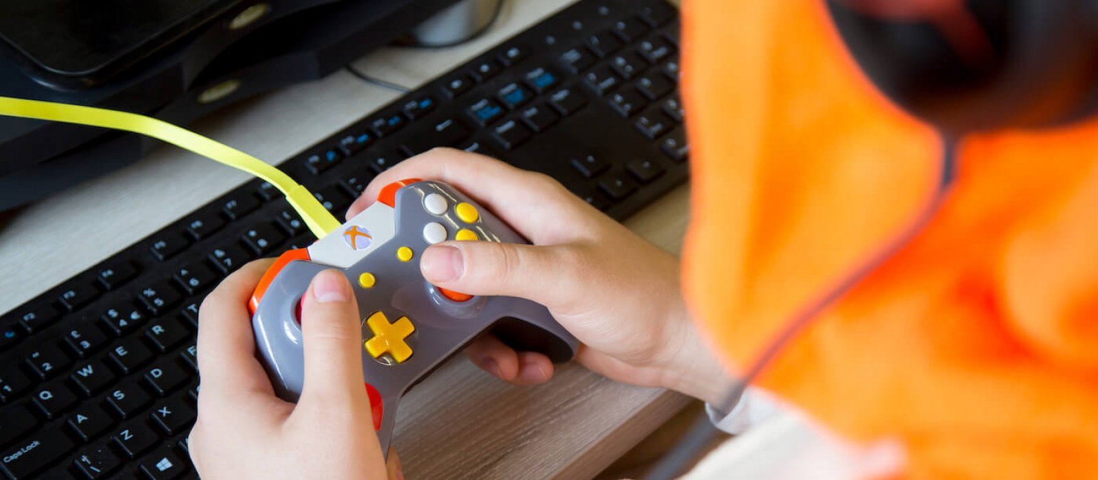 Hands holding a gaming controller in front of a computer keyboard