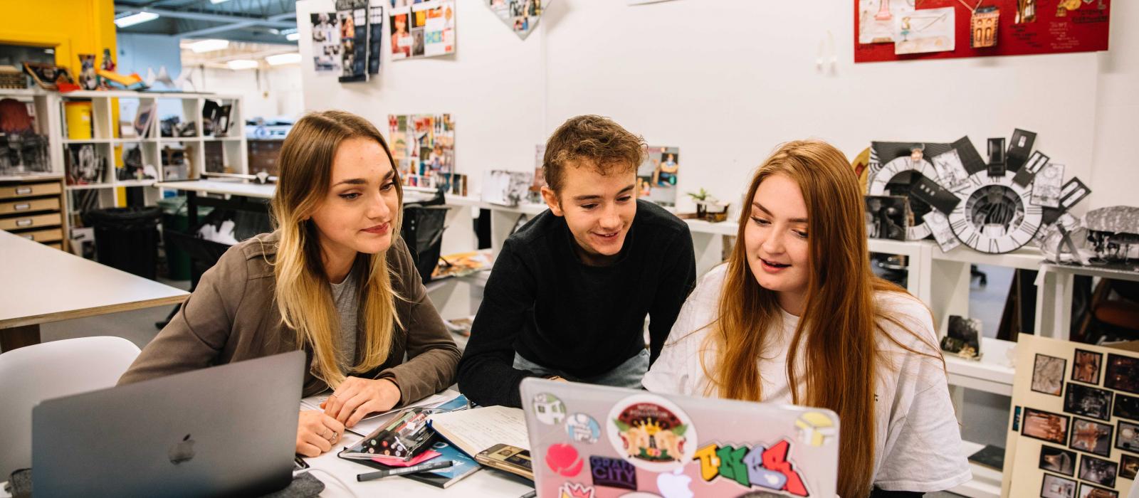 Students gathered around a laptop cover in stickers in the studio.