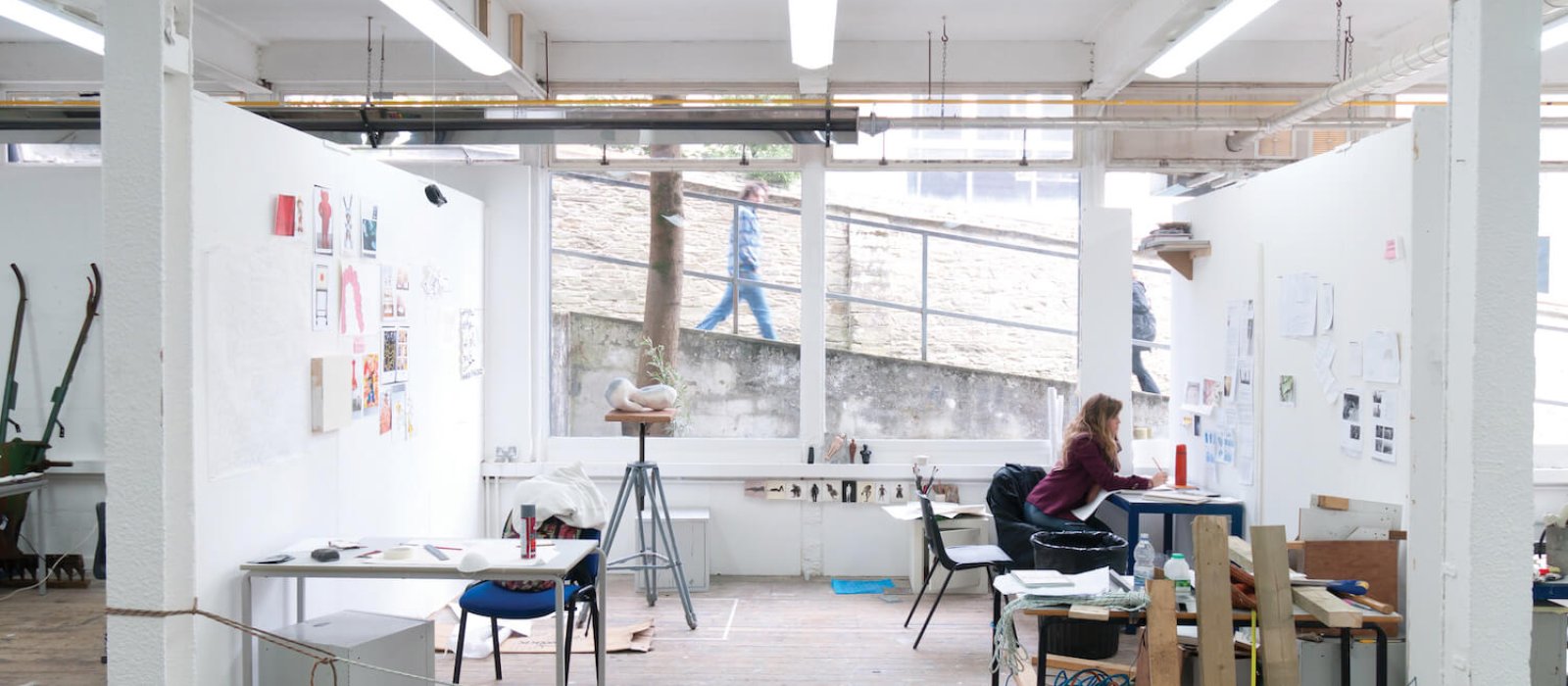 Art student working in studio with large window on Falmouth campus and person walking past and looking in.