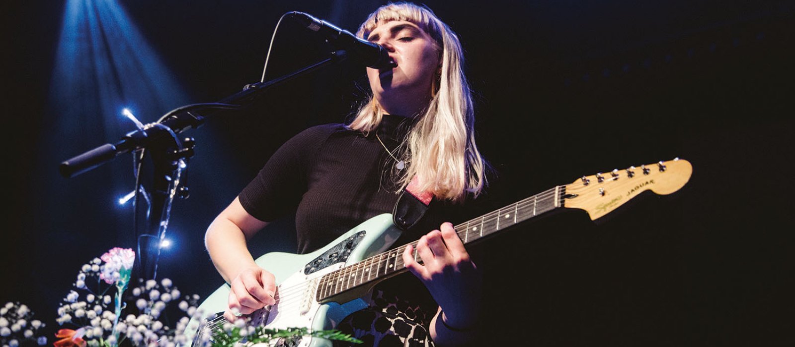 Student singing into microphone on stage and playing guitar