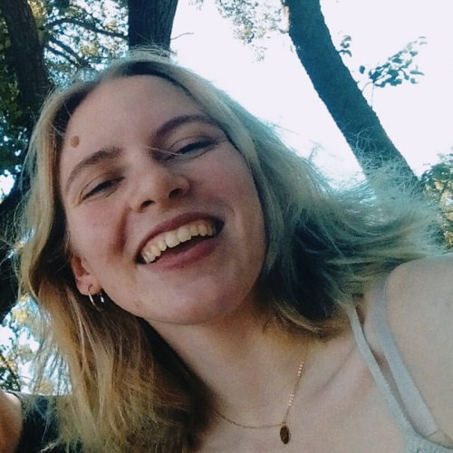 A girl smiling with blonde hair, wearing a necklace
