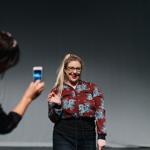 A student smiling while being filmed on a phone by another student