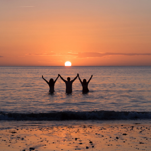 Three Falmouth University students in the sea as the sun is setting
