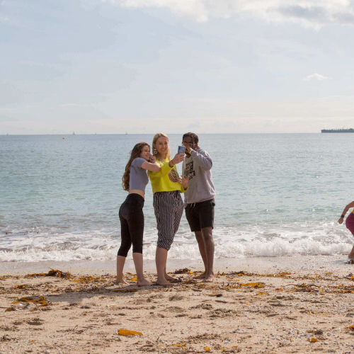 Five Falmouth University students on a sandy beach with the sea in the background