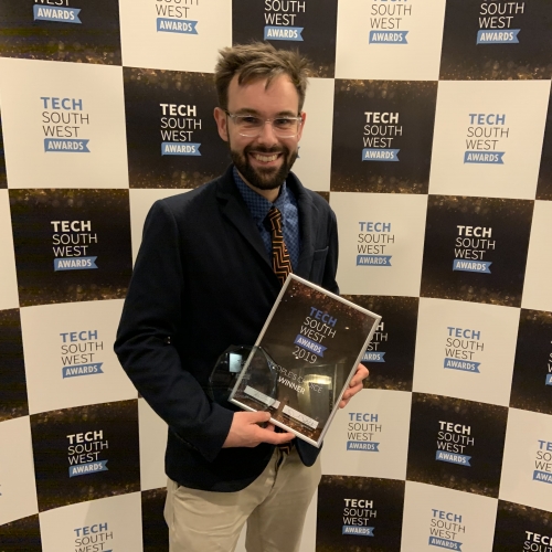 Lecturer holding the Tech South West Award, with a backdrop with branding on it.