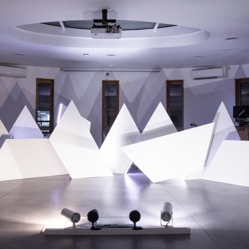 White triangle sculptures in a room lit with purple light