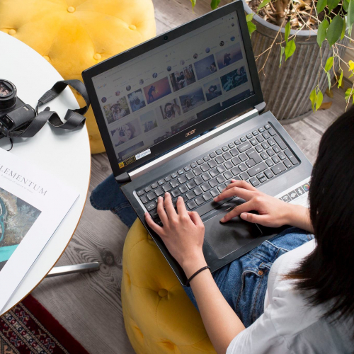 A student working on a laptop next to a white table with a camera and magazine