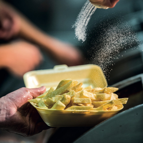 A hand pouring salt on a portion of chips