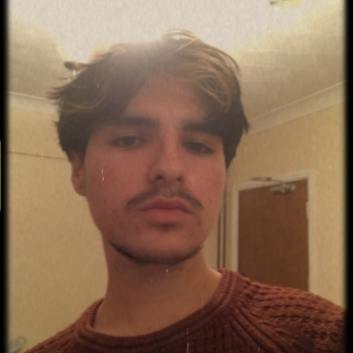 Tomas A Falmouth University student with a moustache, wearing a dark orange jumper