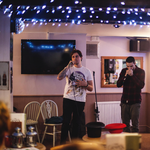 Two Creative Writing students on stage at a poetry slam with blue fairy lights on the ceiling