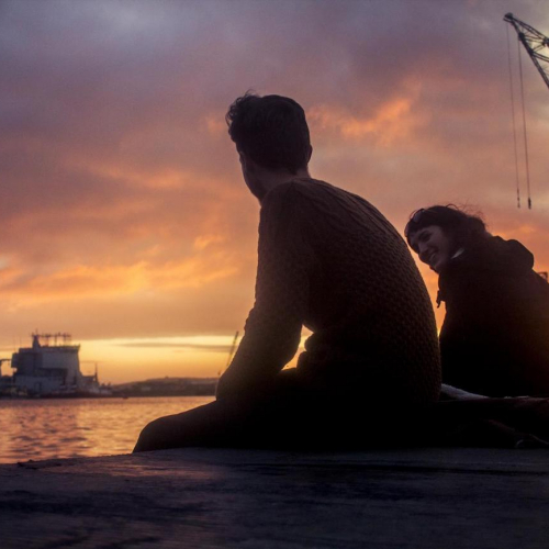 Two students sat watching the sunset with Falmouth docks in the background
