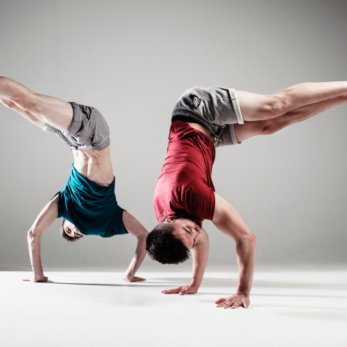 Two dancers doing hand stands and bending at hips so legs are at a right angle mirroring each other.