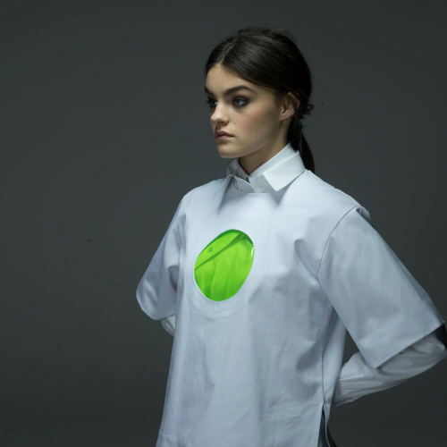 Model in white shirt that has a circular window revealing green fabric underneath.