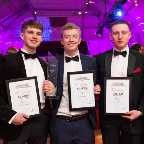 Four male students dressed in tuxedos and holding framed awards