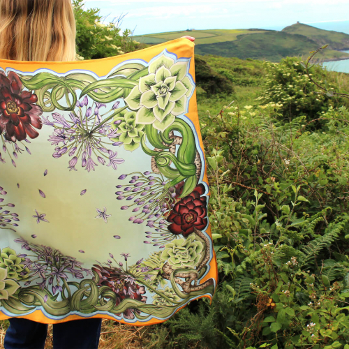 A girl holding a silk fabric design in front of a green landscape with sea