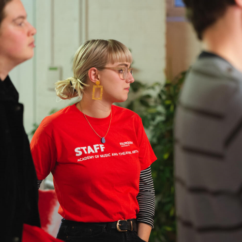 Falmouth Event Management student wearing a red staff t-shirt and yellow earings