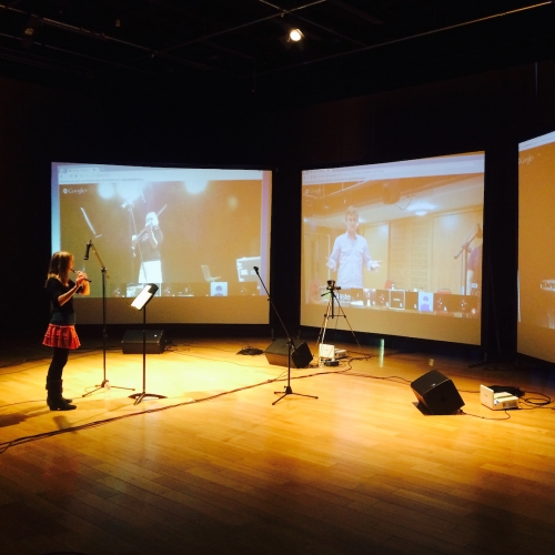 A woman playing the flute in front of three screens