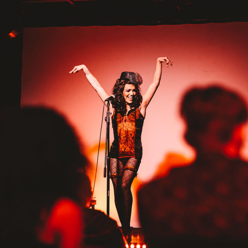 Performer with her hands in her air on stage at Burlesque Night
