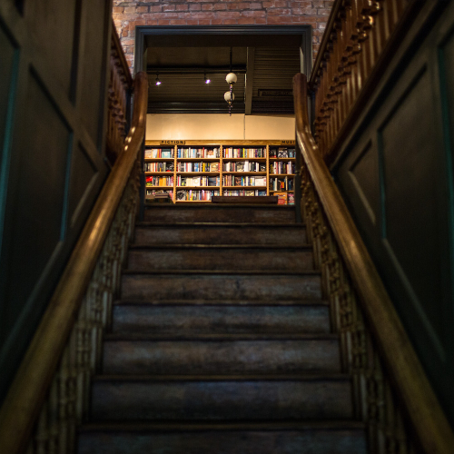 View up a staircase to shelves filled with books.