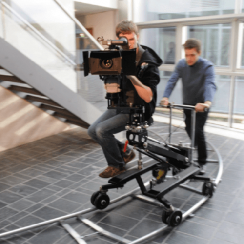 Student behind camera on camera dolly being moved along a track.