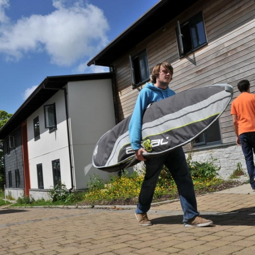 Student carrying surfboard outside student accommodation.