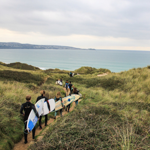 A line of Falmouth University students carrying surfboards heading to the beach