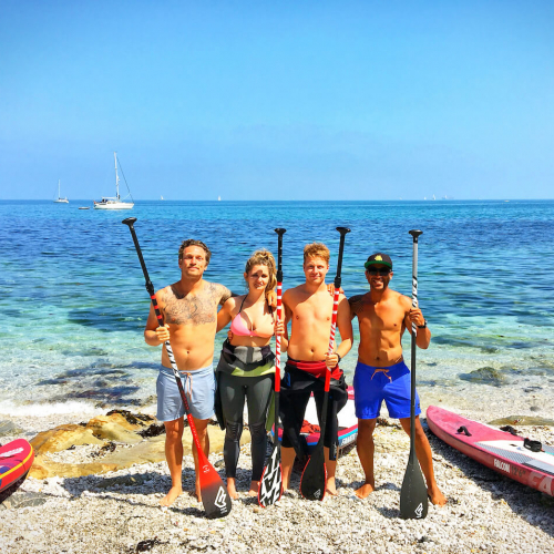 Four people standing on beach with paddles and paddle boards.