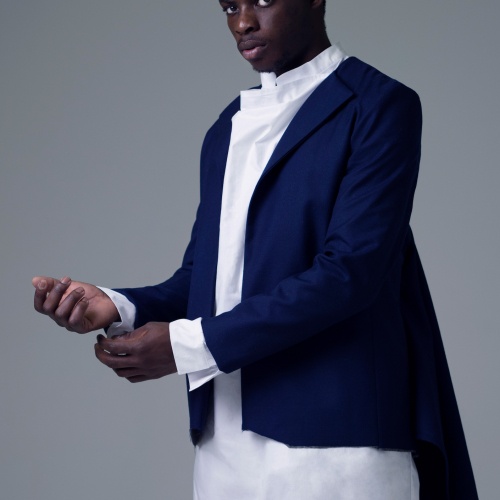 Male model wearing white shirt dress and navy tailored jacket with tails.