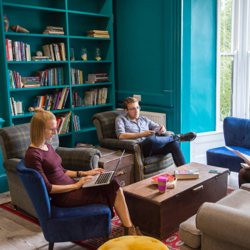 Creative Writing students sat on various armchairs having a discussion in the turquoise coloured writers room on Falmouth campus.