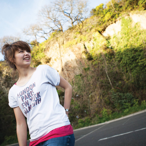A fashion student wearing a white t-shirt while stood outside with bushes and trees