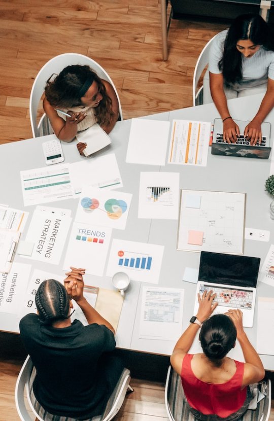 Birds eye view of group of people sat around a table with business strategy papers